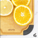 Close-up of an Elihome wood fiber cutting board with color-coded gray silicone corner for fruits, featuring deep juice groove, shown with sliced oranges and lemon.