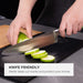 Close-up of a chef's knife slicing zucchini on an Elihome black wood fiber cutting board, demonstrating the surface quality. Text reads: "Knife Friendly. Resist deep cut marks and protect your knives."