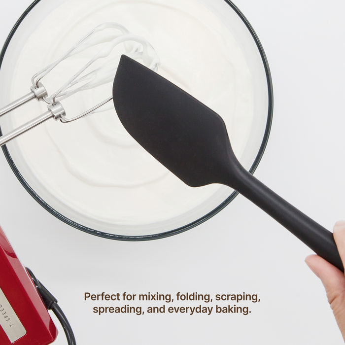 Hand using an Elihome Classic silicone spatula in Black to fold whipped cream in a mixing bowl, perfect for mixing, folding, scraping, spreading and everyday baking
