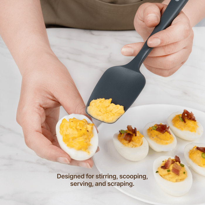 Hand using an Elihome Classic silicone spoonula in Gray to scoop filling onto deviled eggs, designed for stirring, scooping, serving and scraping