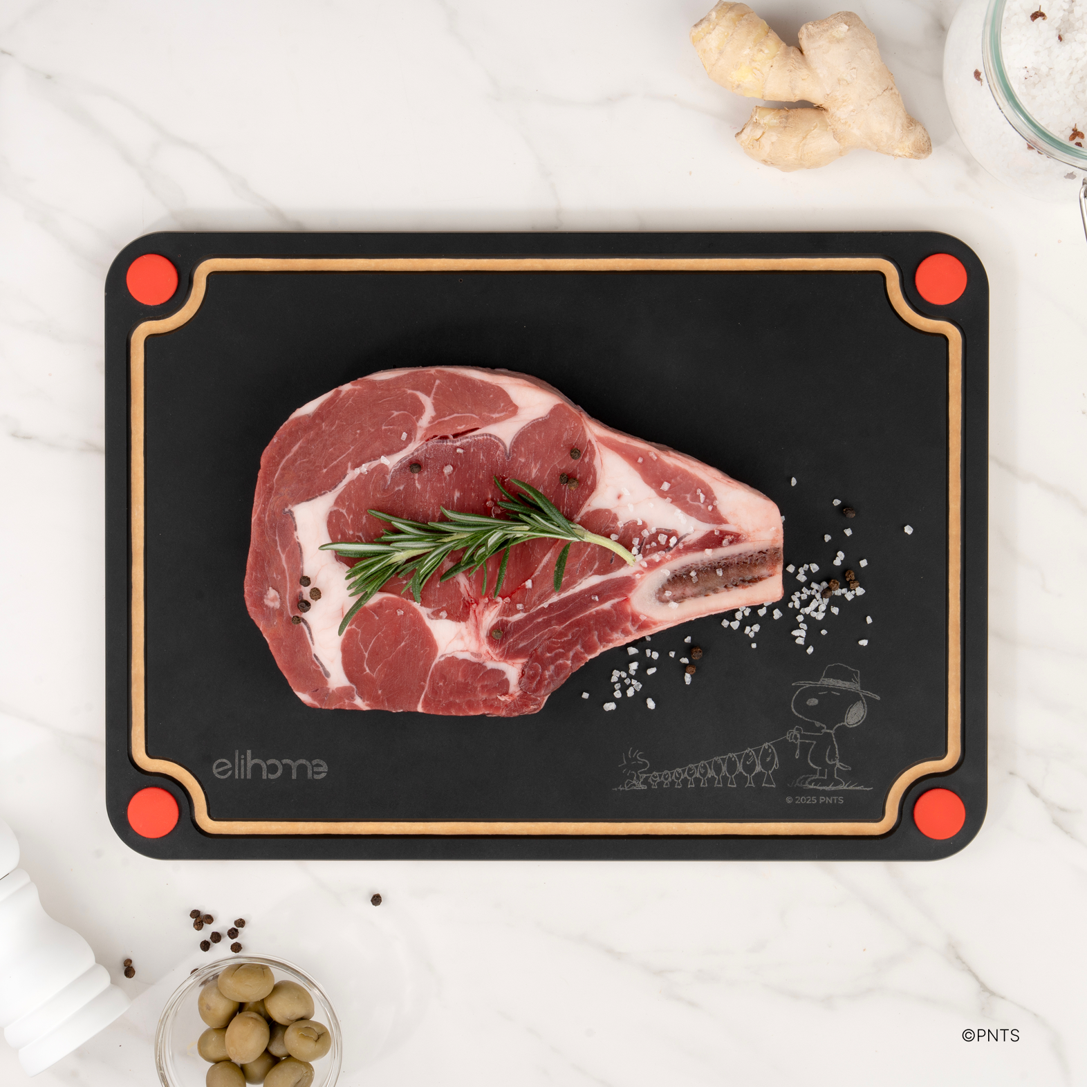 Black side of the Elihome x Peanuts 4-in-1 cutting board with a raw tomahawk steak, rosemary and peppercorns, red corner feet for raw meat