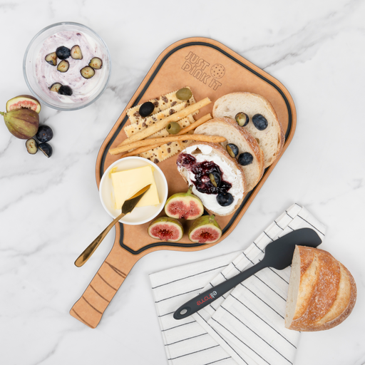 Cheese, figs, berries, breadsticks, and crackers arranged on an Elihome pickleball paddle serving board on a marble countertop
