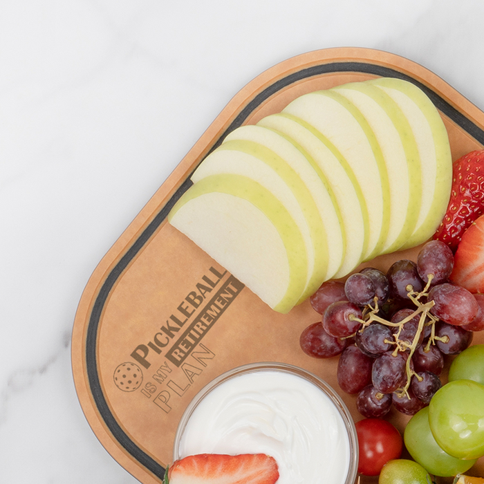 Apple slices, red and green grapes, strawberries, and a bowl of yogurt dip served on an Elihome pickleball paddle board engraved with Pickleball Is My Retirement Plan